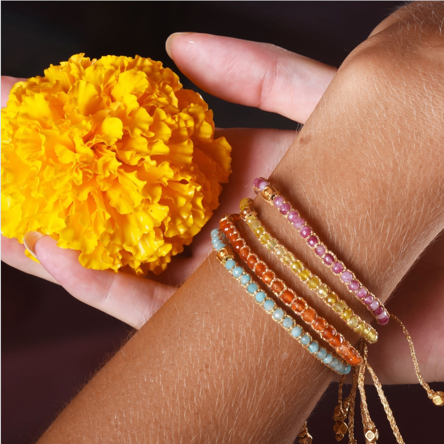 Stacked gemstone bracelets held beside a marigold flower